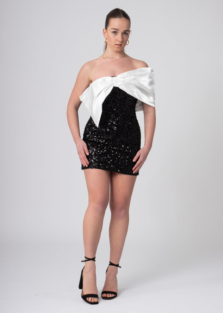 Korte zwarte sequin bandeau off shoulder jurk met grote witte satijnen strik, voor chique feesten.