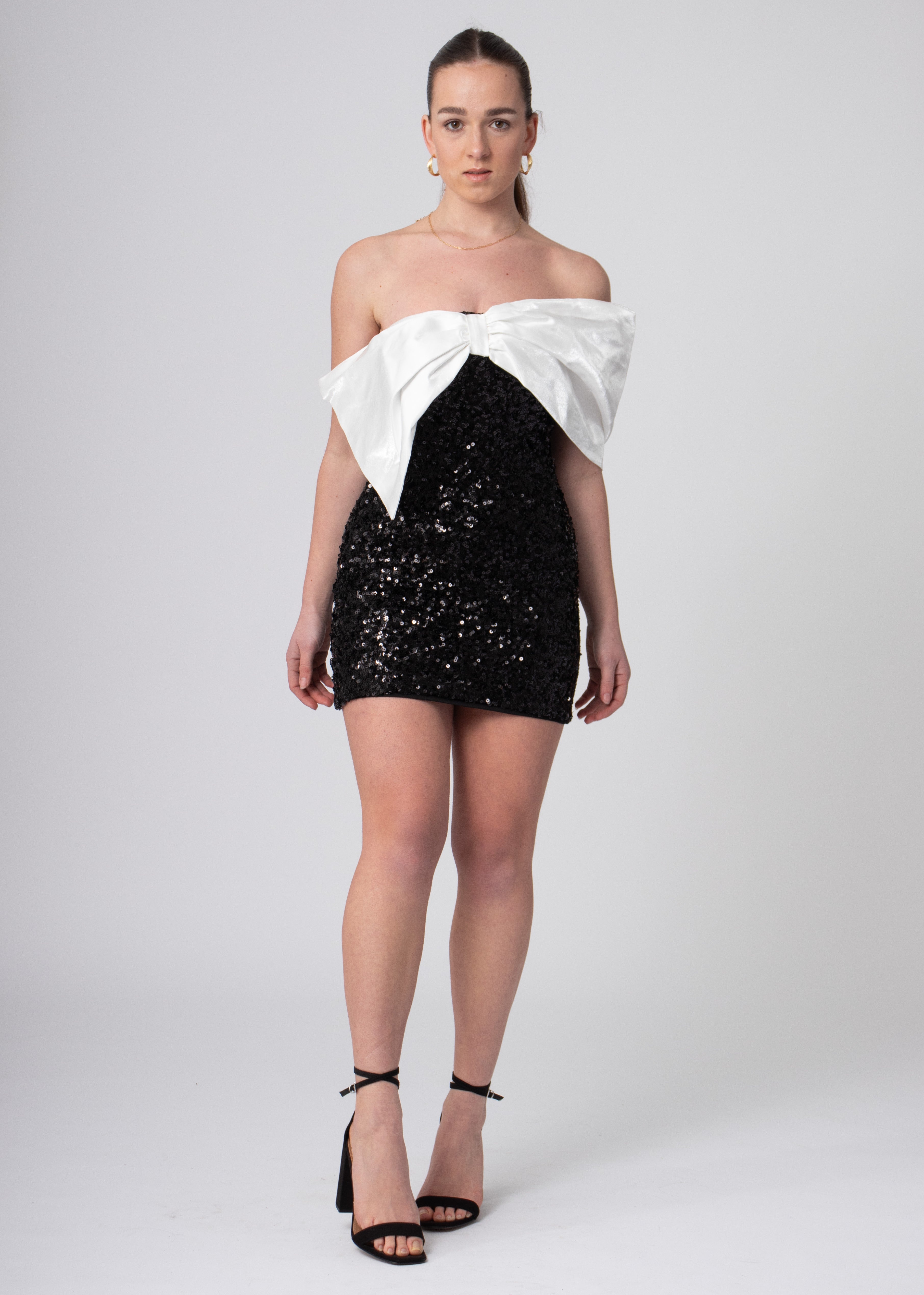 Korte zwarte sequin bandeau off shoulder jurk met grote witte satijnen strik, voor chique feesten.