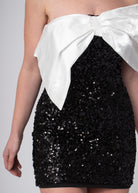 Korte zwarte sequin bandeau off shoulder jurk met grote witte satijnen strik, voor chique feesten.